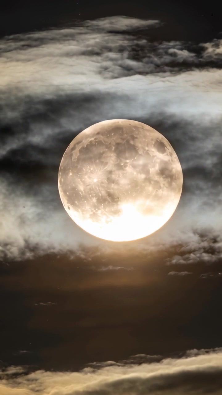 Vídeo vertical: Faixas de nuvens flutuantes afinando, deslocando-se, revelando a face da lua cheia e um halo à noite