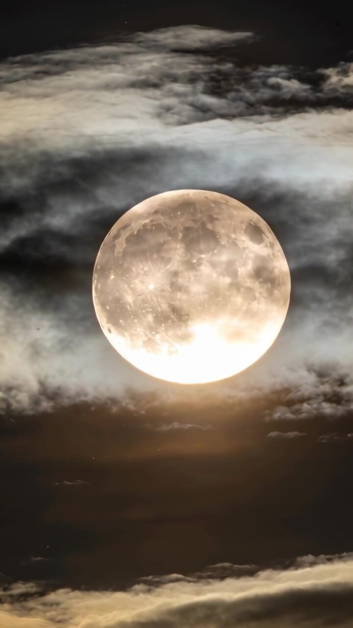 Vídeo vertical: Faixas de nuvens flutuantes afinando, deslocando-se, revelando a face da lua cheia e um halo à noite