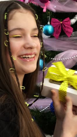 a joyful girl presents a gift box by a christmas tree enjoying a cupcake a joyful girl with braids presents a beautifully wrapped gift box with a yellow polka dot ribbon standing in front of a sparkling christmas tree