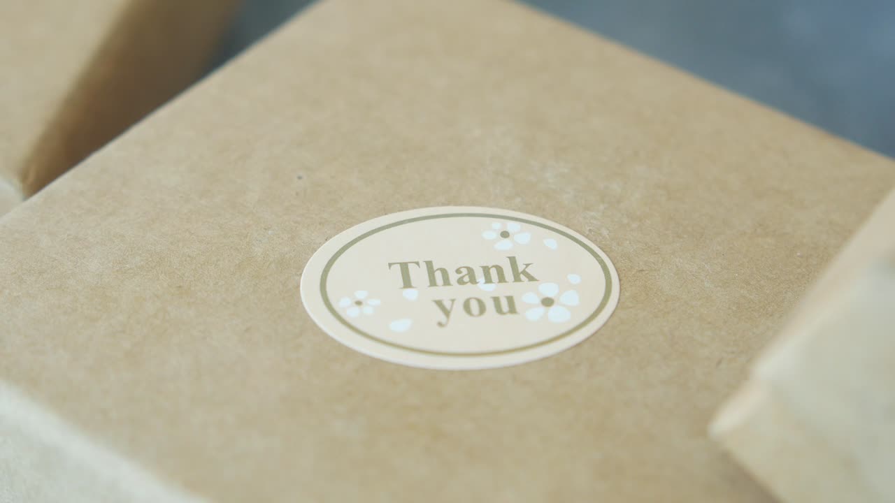 mettendo a mano un adesivo di ringraziamento su una scatola regalo di carta marrone