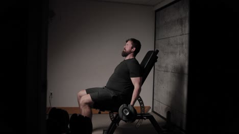 Flexiones-De-Bíceps-Con-Mancuernas-Sentado,-Iluminación-Cinematográfica,-Hombre-Blanco-Vestido-Con-Ropa-De-Gimnasia-Negra