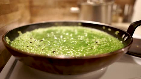 green liquid bubbling in the pan filled with spinach risotto with black himalayan rock salt