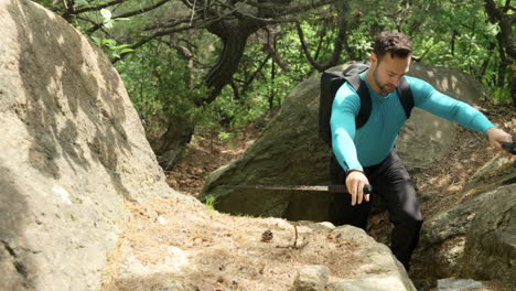 man hiker climbs on huge rocks on the uphill mountain forest wild trail