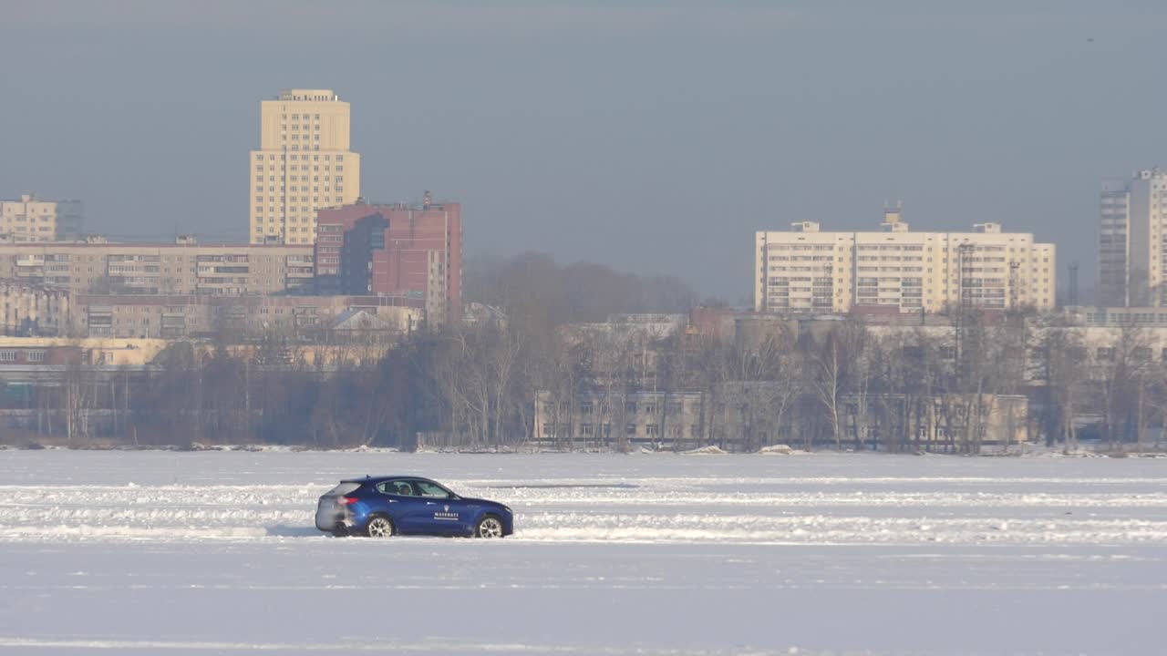 도시 건물 앞의 얼어붙은 호수에서 파란 차를 운전