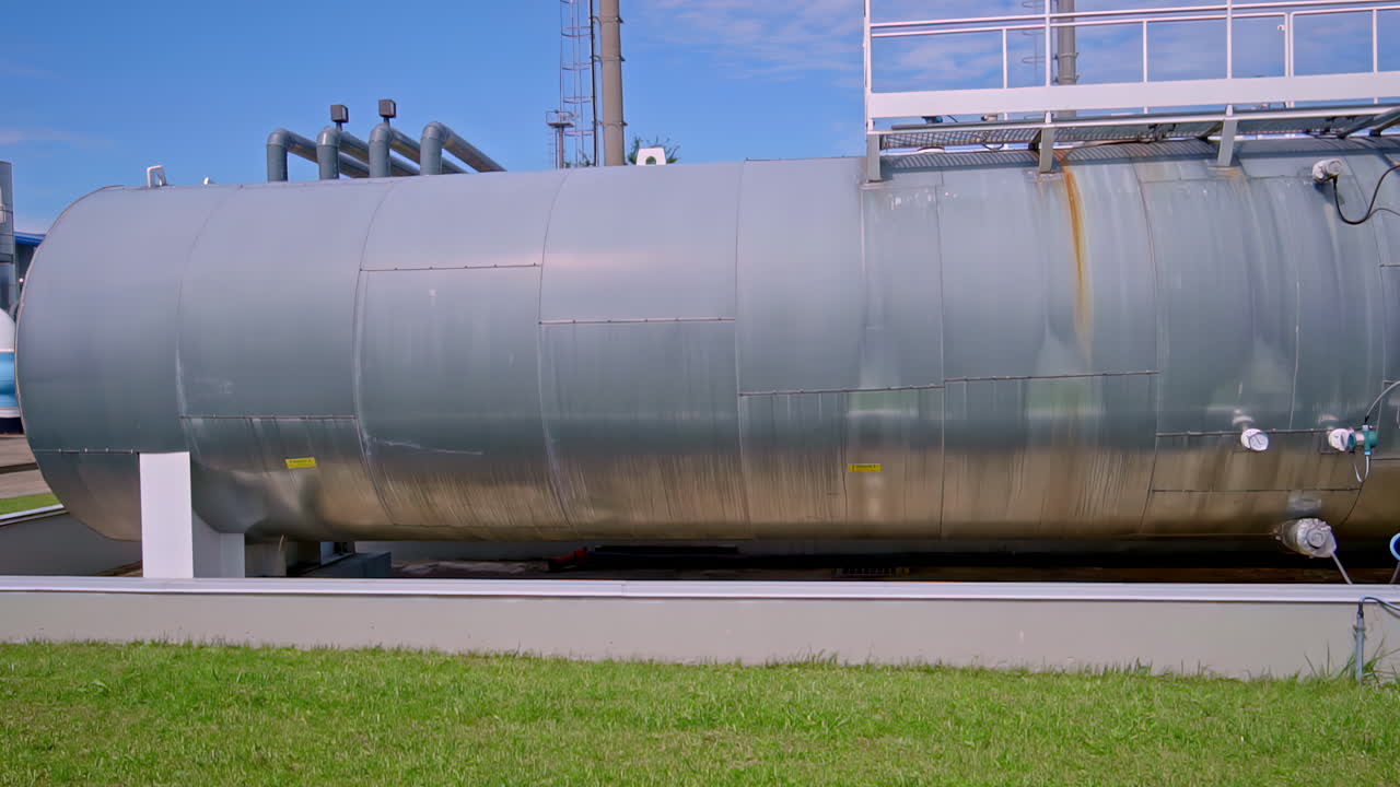 Large cylindrical metal tank with rust stains and access ladder at industrial plant
