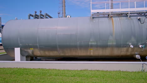large cylindrical metal tank with rust stains and access ladder at industrial plant