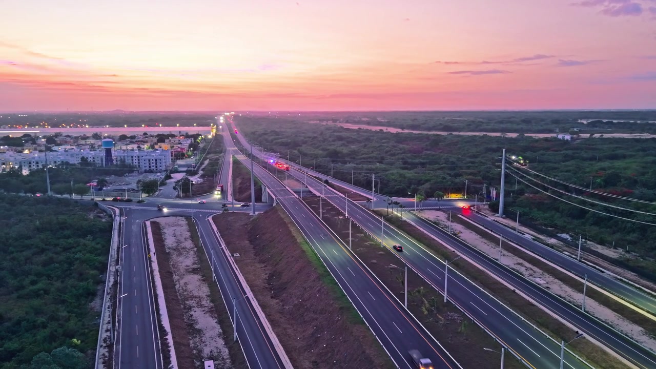 High-angle aerial drone shot flying forward over a modern highway overpass and interchange at sunset, capturing trucks and vehicles driving on paved lanes