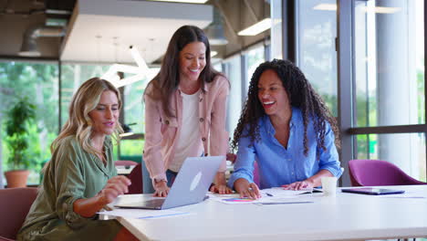 equipo de negocios femenino multicultural sentado en un escritorio con una computadora portátil en la oficina colaborando en un proyecto