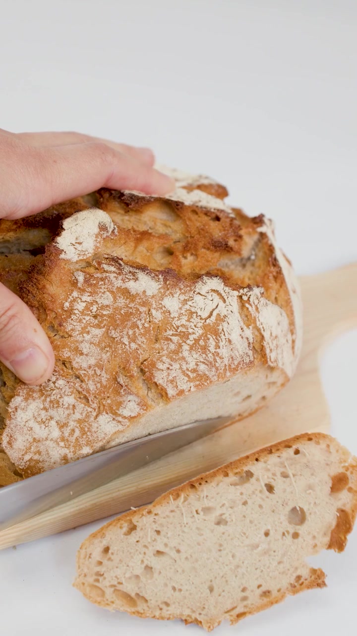 Close-up of hands using a knife to slice artisan sourdough bread on white background.