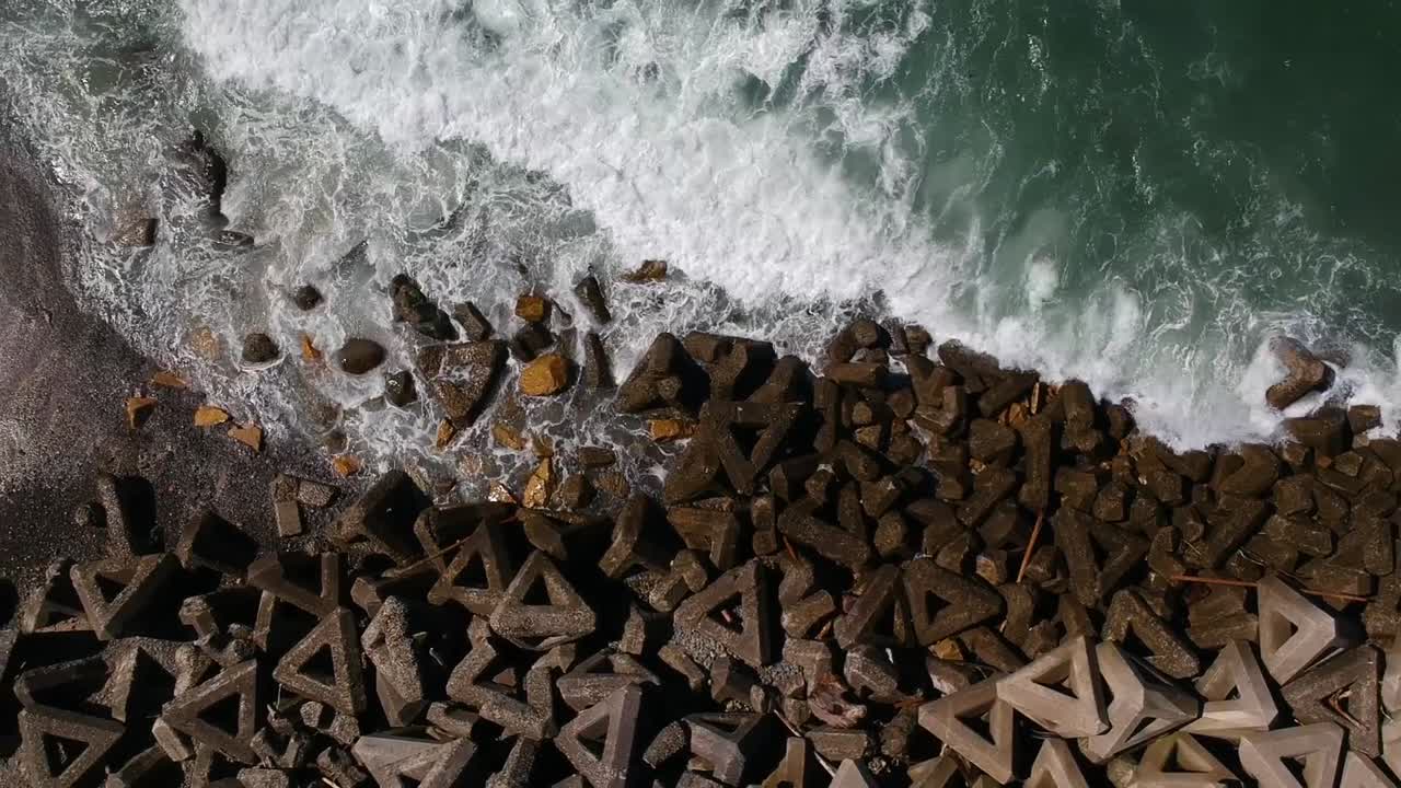 Dronepanorering ovenfra og ned over kystens bølgebrydere med bølger, der brager ind i Wakayama