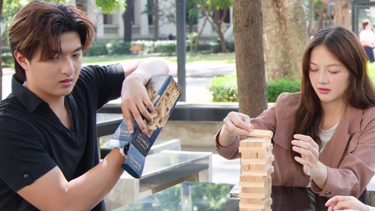 キャンパスの敷地内で、若いタイ人学生たちが屋外で木製ブロックタワーゲームを楽しんでいます。