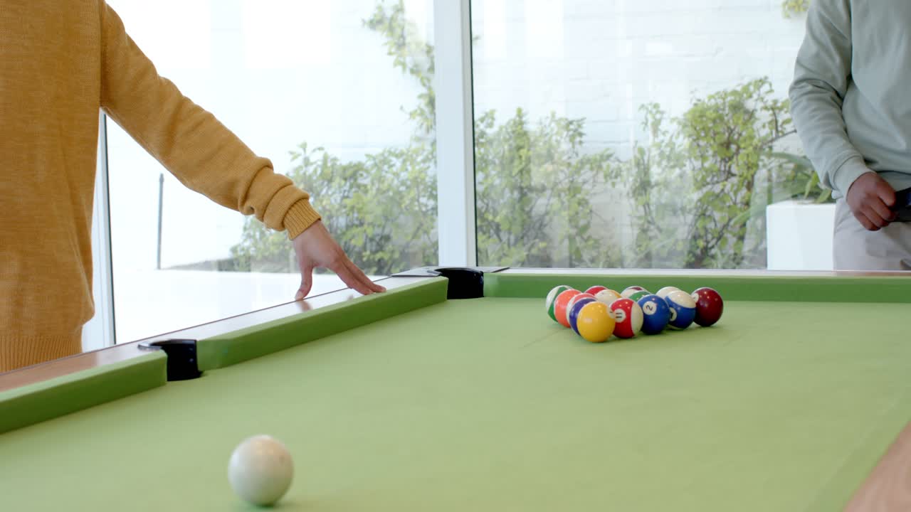 After game start, diverse male friends stepping up to rack balls at pool table before breaking