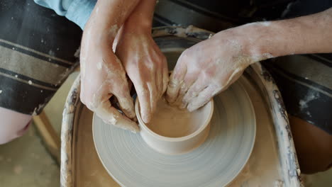 two people making a bowl on a pottery wheel