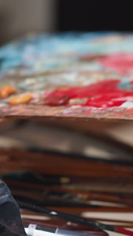 artist puts color palette on round table in studio closeup. man leaves wooden board with oil paint pigments in shop. supplies for art manufacturing