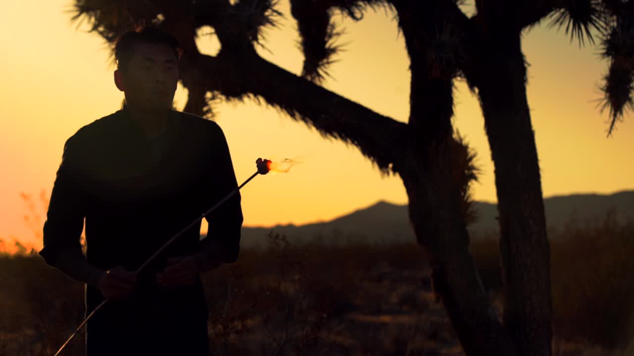 slow motion side silhouette of man blowing fire in the desert at sunset