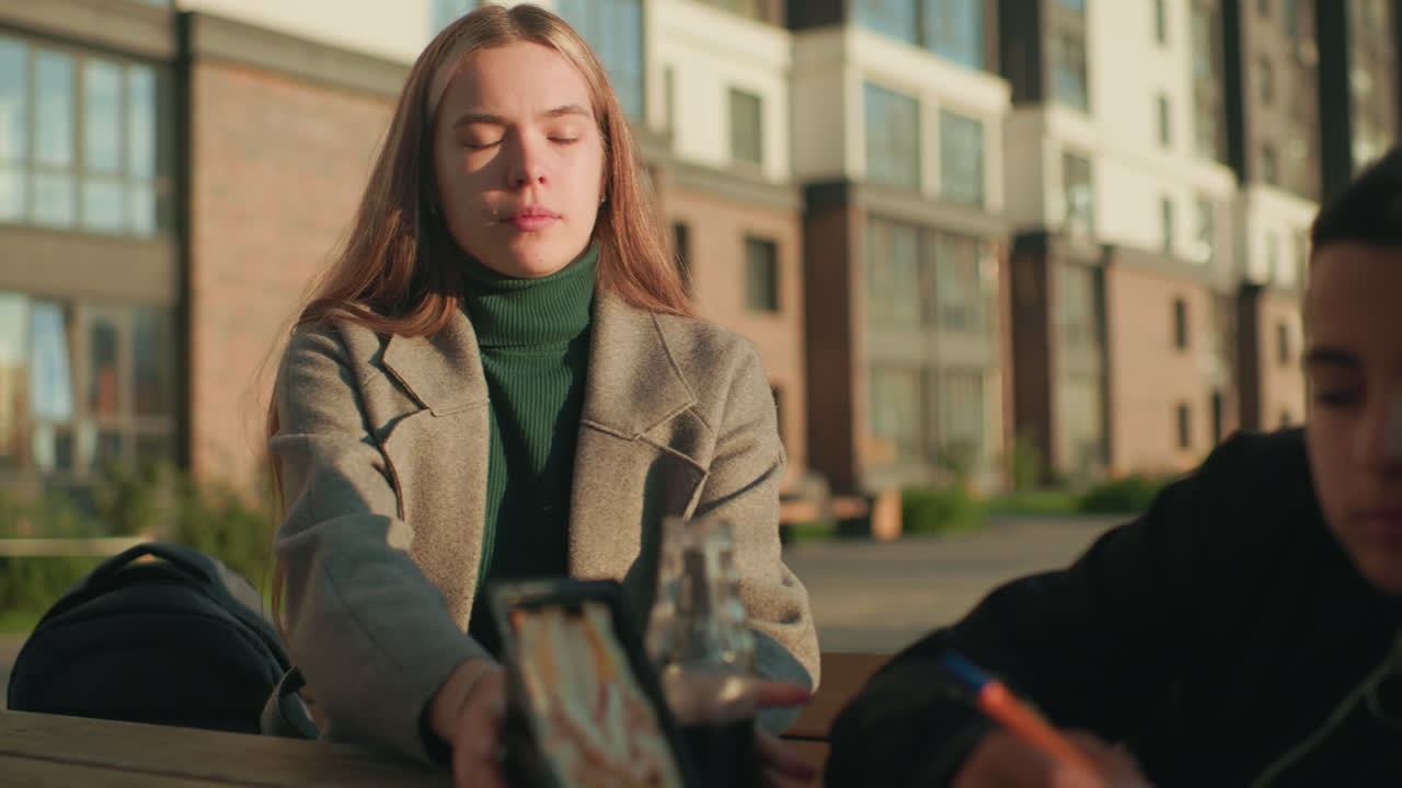 Lady offers snack and drink to unhappy child while seated outdoors, child remains disinterested with dull expression, mother gently holds food and beverage
