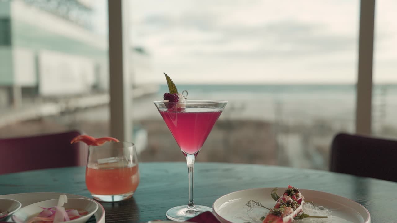 Vibrant red cocktail resting on a table overlooking the ocean