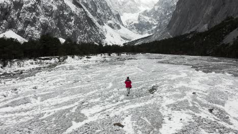 Excursionista-Explorando-El-Antiguo-Valle-Del-Río-Glaciar-En-Las-Montañas-Nevadas-De-Yulong,-Vista-Aérea