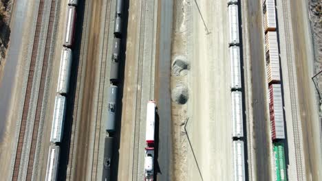 bird's-eye view truck forward drone shot flying over railroad station in a desert environment on a sunny day with cargo and tank tain