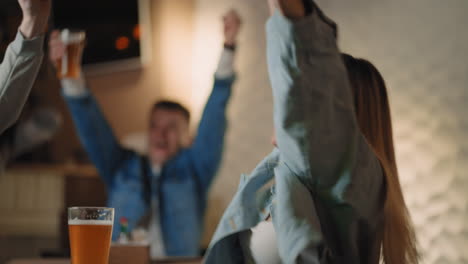 Close-up-of-a-group-of-male-and-female-friends-sitting-together-in-a-bar-and-watching-a-broadcast-on-TV-enjoying-a-goal-scored-shouting-and-hugging.-in-football-basketball.