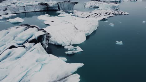 Drohnenaufnahme-Wunderschöner-Schwarz-weißer-Eisberge,-Die-In-Einer-Lagune-In-Island-Schwimmen