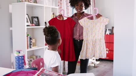 mother helping daughter to choose clothes for school in bedroom