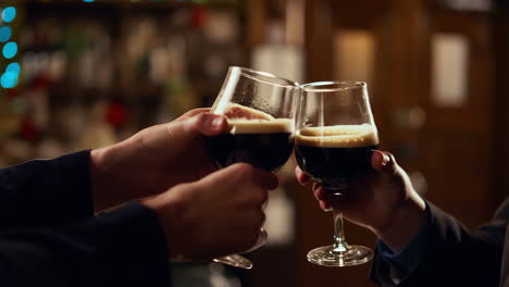 two people toasting with dark beer glasses in a bar