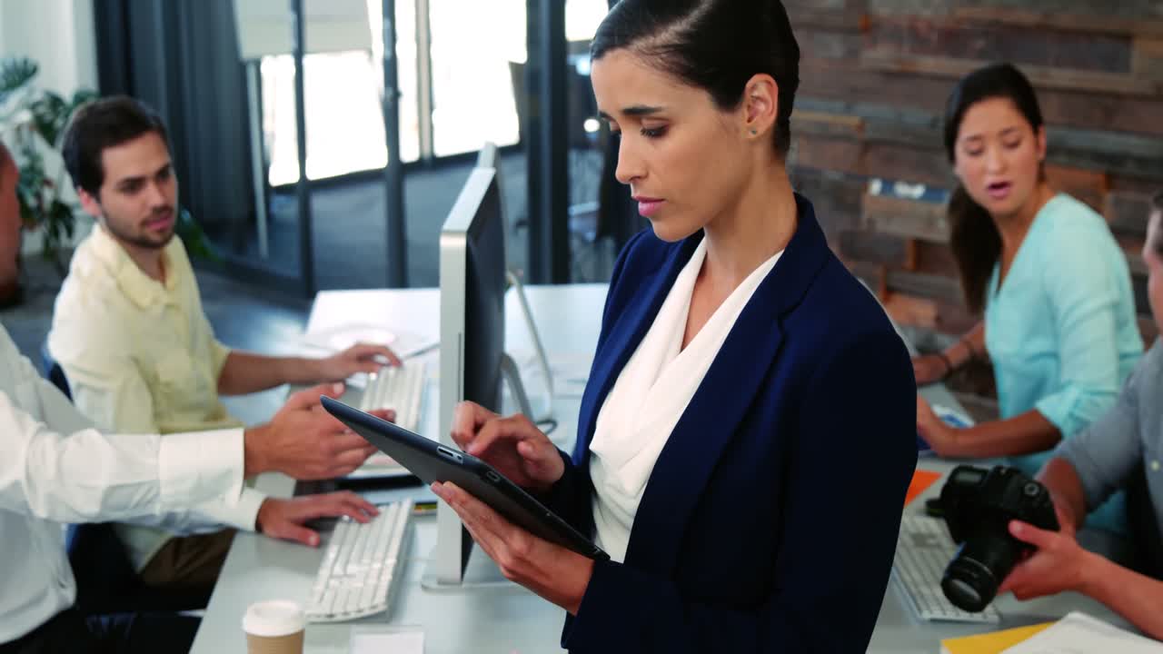Executiva usando tablet digital enquanto um colega trabalha na secretária