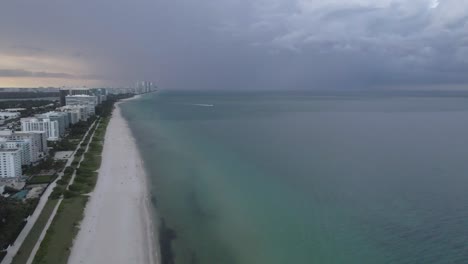 Dark-heavy-sunset-cloud-over-Surfside-beach-at-dusk,-Miami-aerial