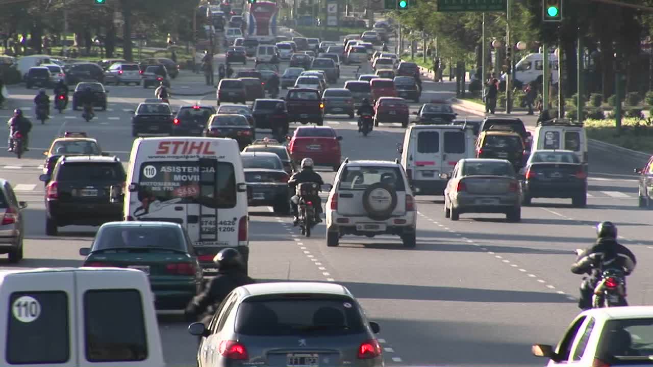 una calle de la ciudad está repleta de automóviles, motocicletas y algunos peatones