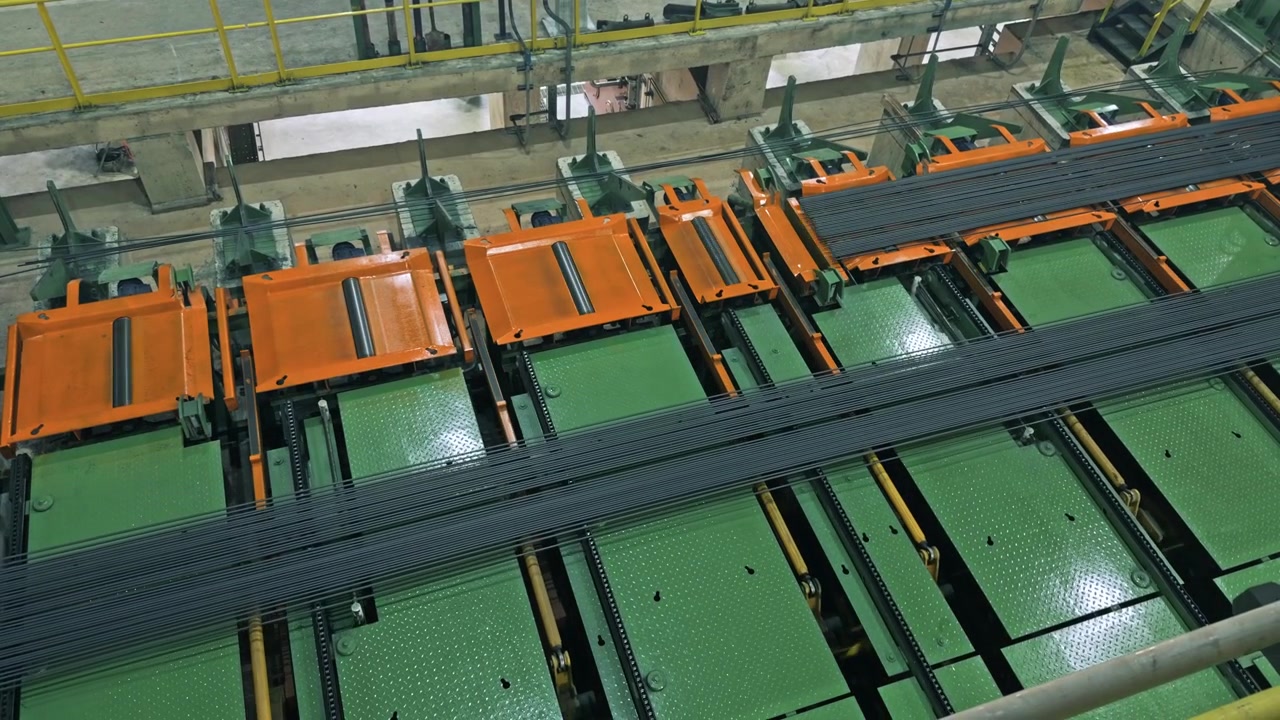 Ecoacero steel rod factory with orange and green rolling mill machinery, yellow safety railings and steel rods on conveyor seen from directly above. Dominican Republic. Aerial drone top down.