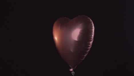 Shining-heart-shape-balloon-ascends-isolated-on-black-background