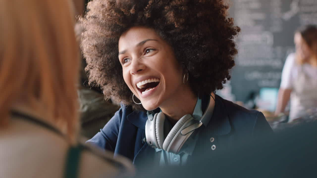 bella donna di razza mista con capelli afro che chiacchiera con un'amica in un caffè, socializza, gode della conversazione, passa il tempo in un caffè affollato.