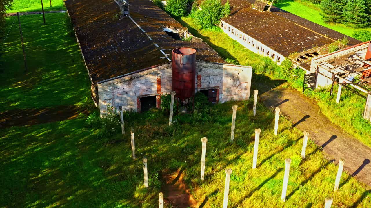 Old Abandoned Farm Buildings and Tall Concrete Posts on Overgrown Green Field