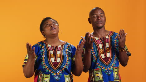 Ethnic-couple-praying-to-God-with-arms-spread-on-camera