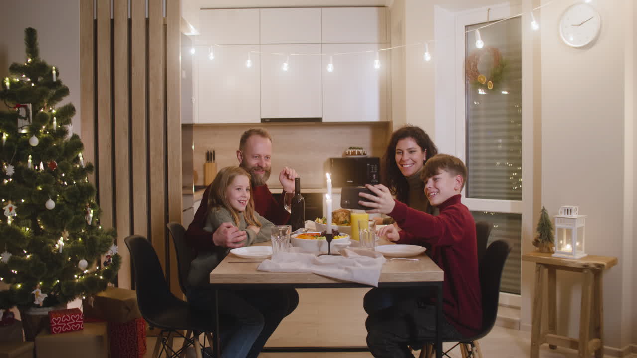 Blond Boy Sitting With His Sister And Parents At The Christmas Dinner Table Uses A Smartphone To Make A Family Selfie 1