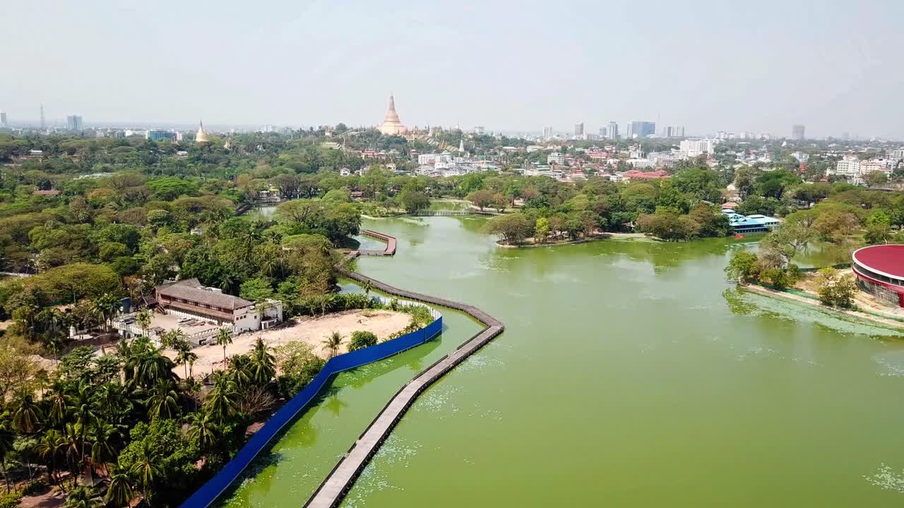 una impresionante vista aérea del lago kandawgyi y sus exuberantes alrededores con la icónica pagoda shwedagon en rangún, myanmar. la escena presenta una vegetación vibrante, reflejos de agua y aspectos urbanos destacados
