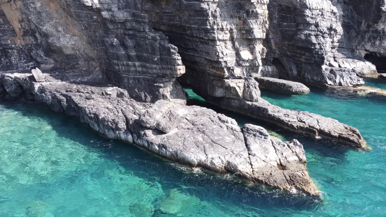 Orbit aerial video over turquoise water and stunning rock formations of Aspes Black Beach, South Crete, Greece