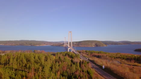 aerial drone view towards a bridge, between hills, lakes and forest, on a sunny spring day, in hoga kusten, vasternorrland, sweden