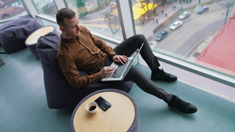 man working with laptop while sitting on armchair near panoramic window