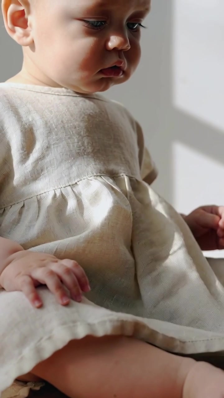 Video verticale: Mani adulte che sistemano un vestito di lino alla finestra di casa, un bambino che tocca il vestito per calmarsi