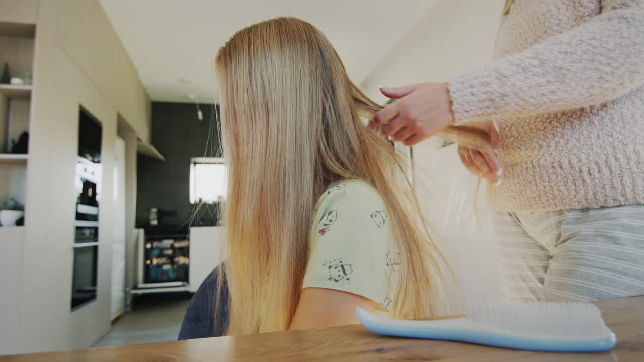 Woman untangles her daughter's long hair. Hair is very tangled and hard to comb