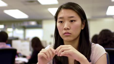 a young woman appears deep in thought in a bustling office environment filled with coworkers. her focused expression suggests she is considering important tasks or decisions.
