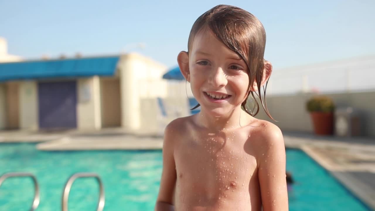 한 어린 소년이 수영장 앞에서 물을 뚝뚝 흘리며 그가 얼마나 즐거운 시간을 보내고 있는지에 대해 이야기하면서 미소를 짓고 웃는다