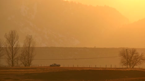 Cars-driving-along-a-country-road-against-a-backdrop-of-mountains-and-sunset