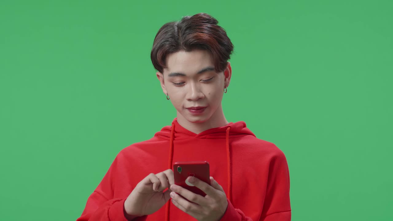 Happy Asian Transgender Male Enjoy Using Mobile Phone While Standing On Green Screen In The Studio