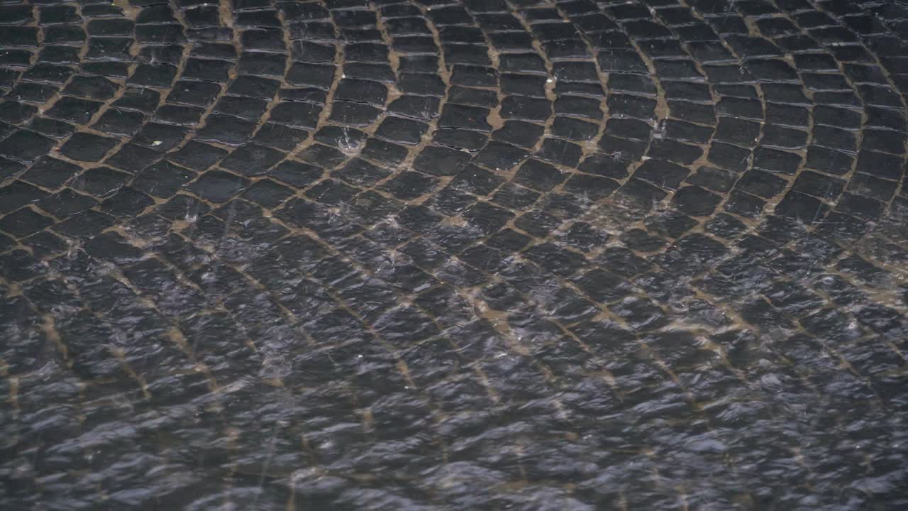 water are flowing through the pavement in the city. Raindrops are turning into a stream of water that flowing up the street