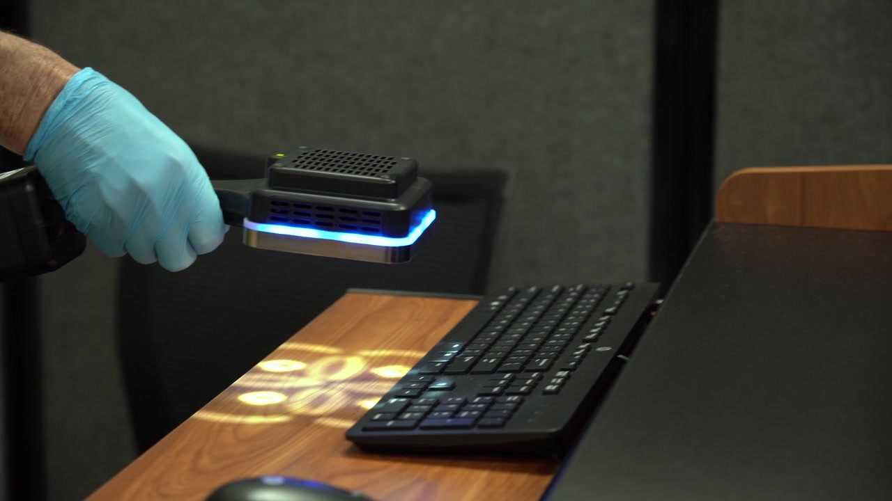 Worker uses UV light to disinfect furniture during the COVID-19 pandemic, demonstrating enhanced sanitation, infection control, workplace safety protocols, and measures to reduce viral contamination.