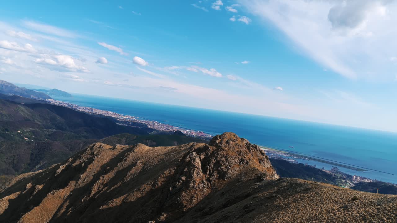 Stunning aerial footage from Mount Praglia with a sweeping view over rocky ridges, the Ligurian coastline, and the Mediterranean Sea. Dutch angle and centered forward-facing framing