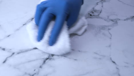 cleaning a marble countertop with a white cloth and blue gloves